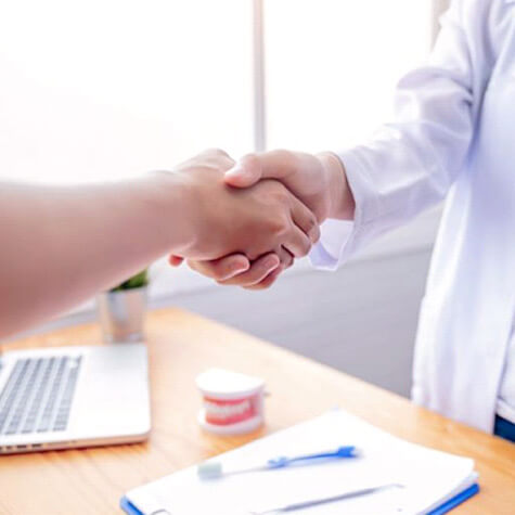 two people in dental office, shaking hands above desk